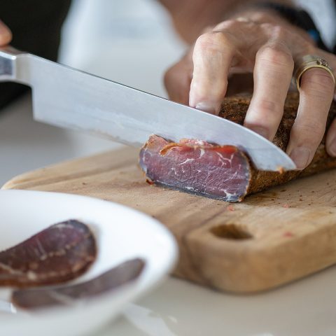 Chef preparing a meal in a kitchen, slicing pieces of pastirma on a wooden cutting board