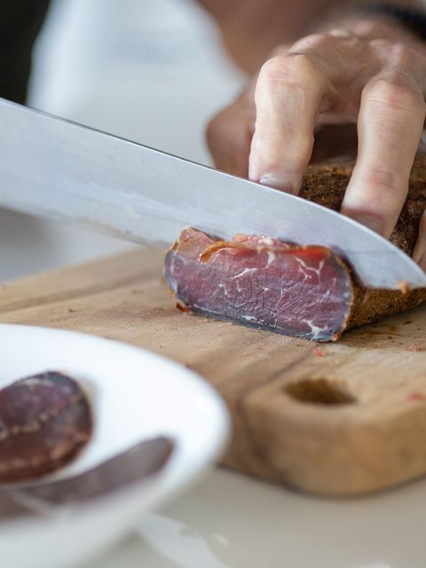 Chef preparing a meal in a kitchen, slicing pieces of pastirma on a wooden cutting board Chef preparing a meal in a kitchen, slicing pieces of pastirma on a wooden cutting board
