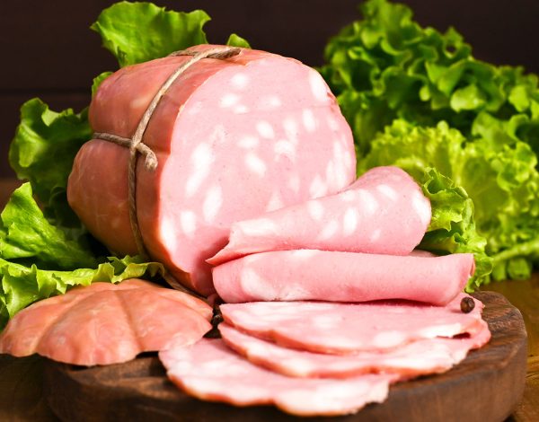 big Italian Whole block of mortadella on a wooden plate. Traditional big sausage and black pepper pistachios Region Emilia Romagna and the city of Bologna. Top view. Copy space